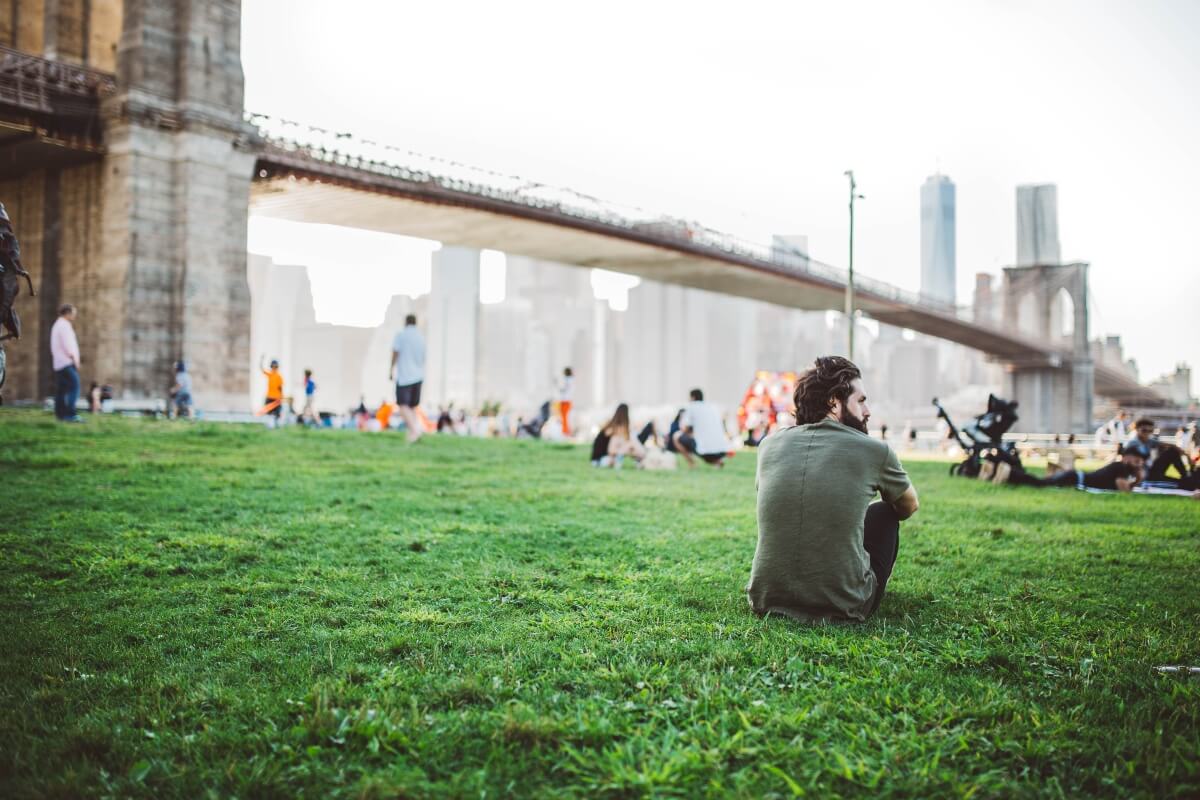 man sat on green space near broklyn bridge